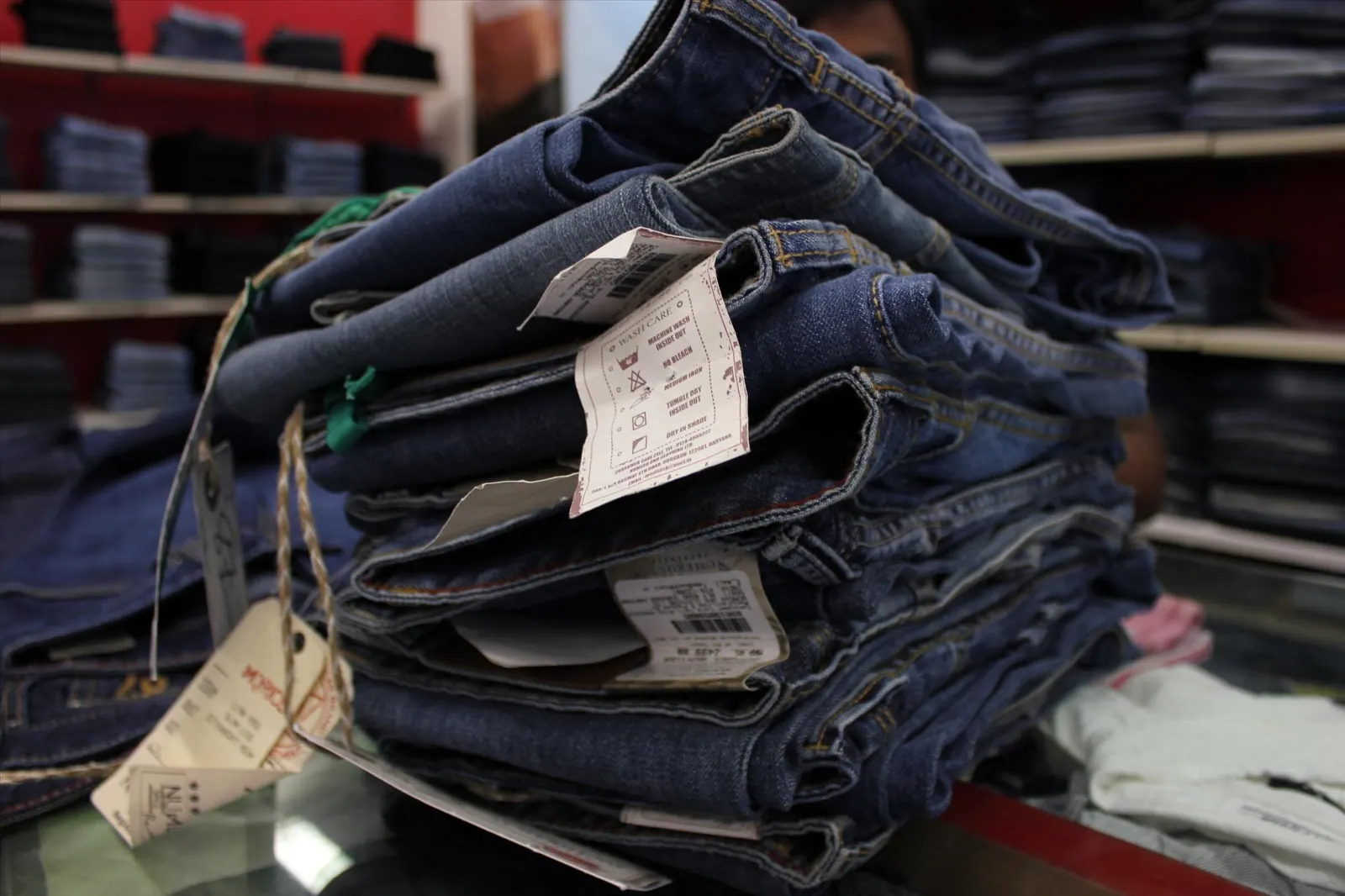 Stack of folded blue jeans with hang tags, showing slightly different shades