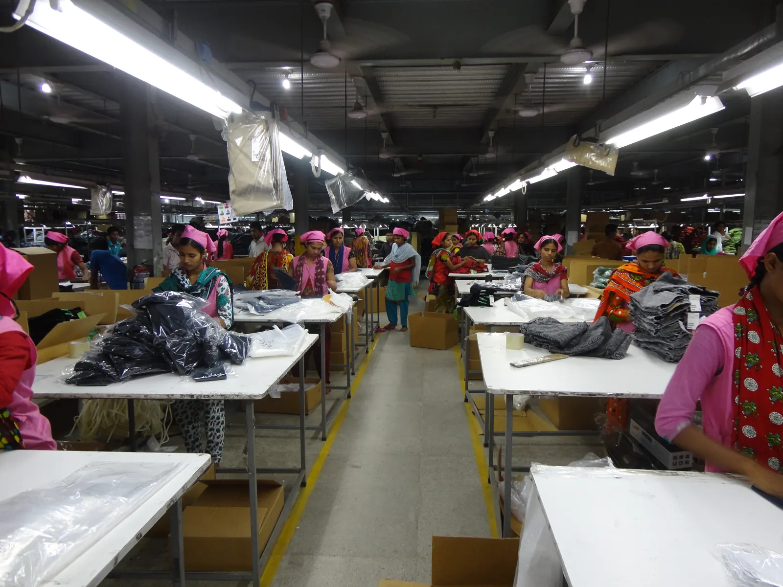 Workers checking washed denim jeans by hand on long inspection tables