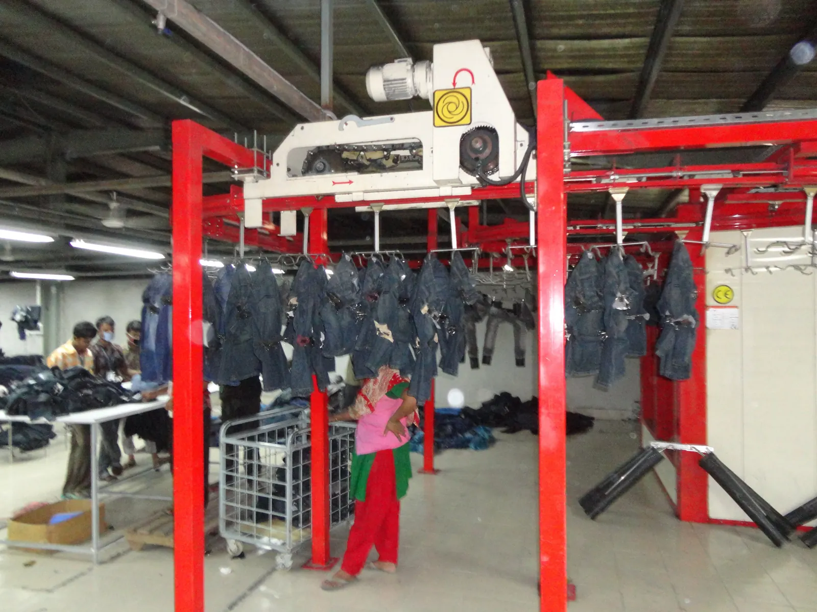 Washed denim jeans hanging on an overhead garment conveyor in a finishing plant