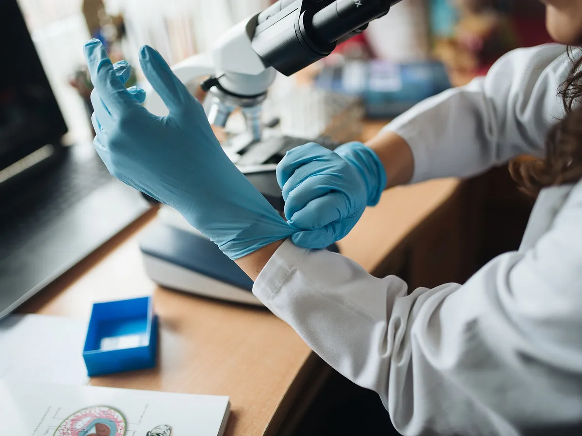Laboratory technician pulling on blue protective gloves at a lab bench