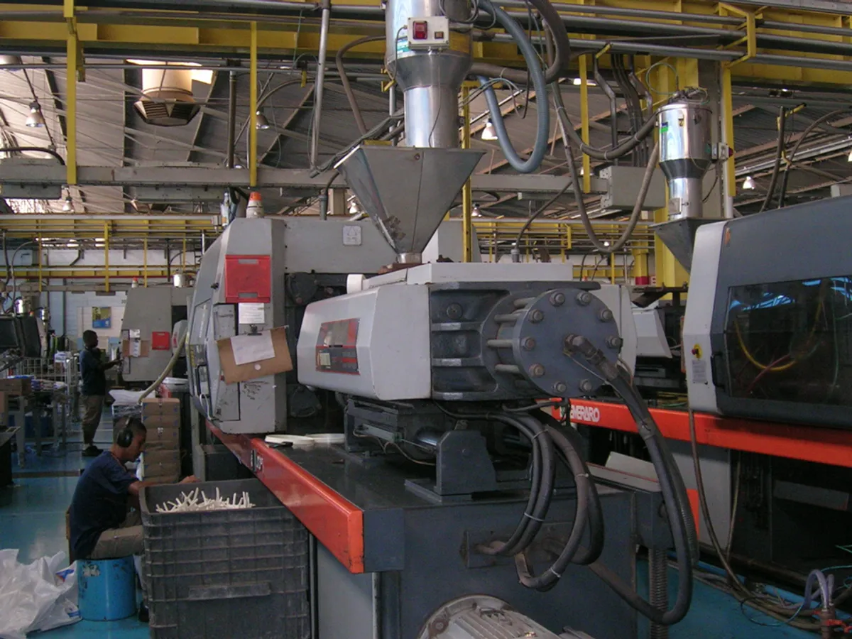 Injection moulding machines in a plastics plant, with an operator sorting moulded parts by hand beside the press